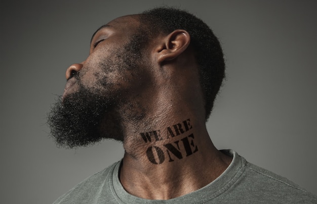 Close up portrait of a black man tired of racial discrimination has tattooed slogan we are one on his neck. Concept of human rights, equality, justice, problem of violence and racism, discrimination.