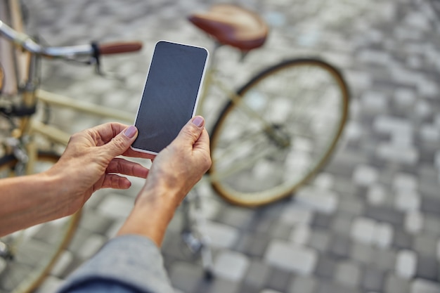 Close up portrait of black screen of modern mobile phone in woman hand isolated on road in the park