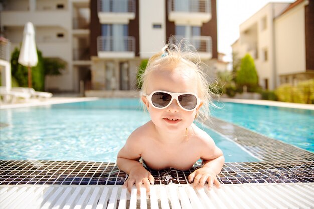 The close up portrait of a blonde smiling toddler girl, getting out of swimming pool.