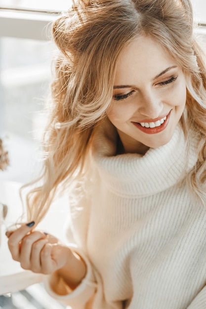 Close up portrait of blonde young woman in sweater. She is happy.