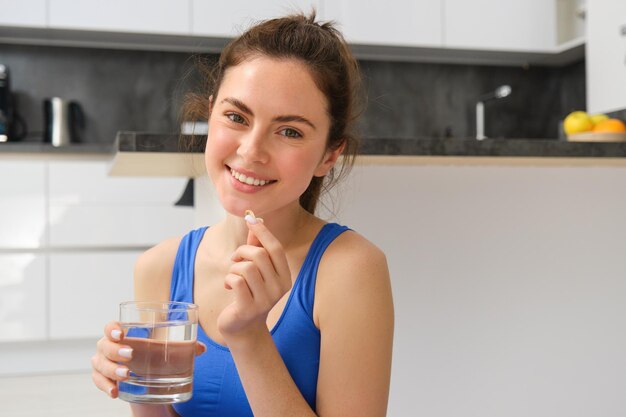 Photo close up portrait of brunette fitness woman taking dietary supplements vitamins and glass of water