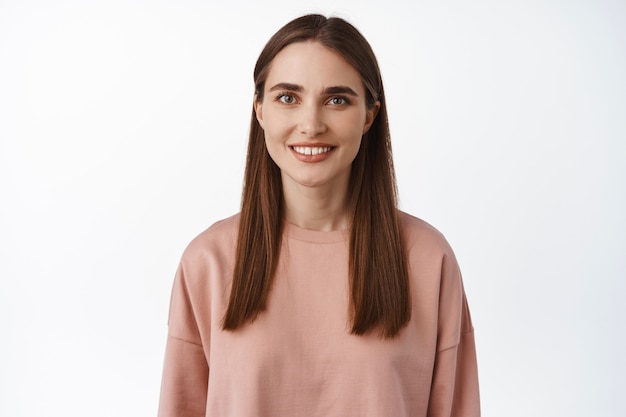 close up portrait of brunette girl smiling happy on white teeth, looking carefree , standing in pink sweatshirt, casual relaxed pose on white