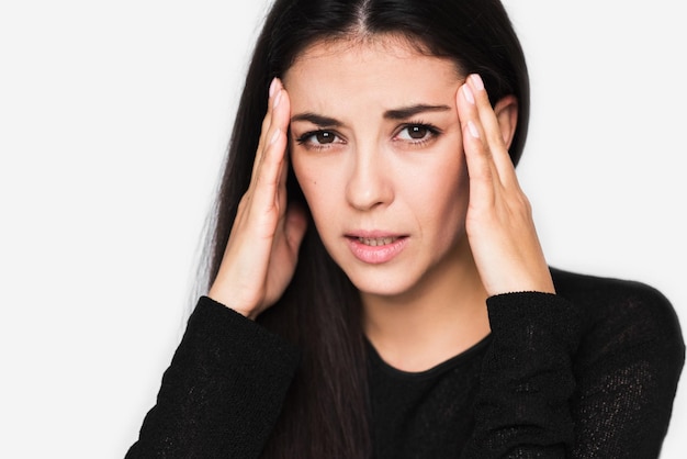 Close up portrait of brunette pretty woman with headache touching her face look up Beautiful woman stressed and worry in black sweater on light grey background Health care and medicine