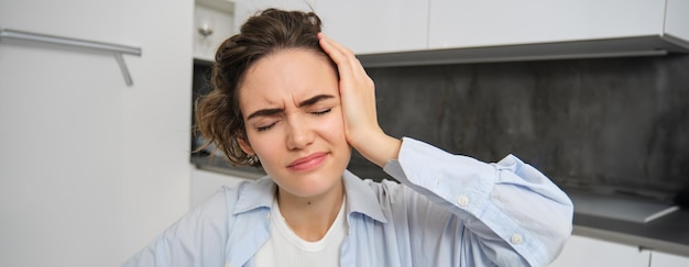 Close up portrait of brunette woman touches her head feels dizzy has migraine or headache grimaces