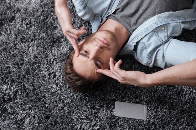 Close up portrait of a casual man lying on a carpet and intensely thinking