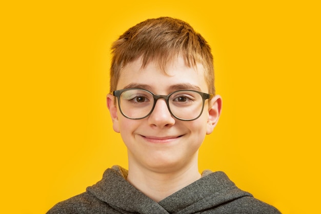 Close up portrait of caucasian brunette boy with brown eyes with glasses on yellow background Teenager with brown hair looks into the camera and smiles