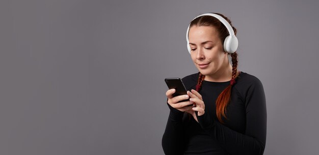 Close up portrait of caucasian female podcast or music listening on grey background. listening music in headphones