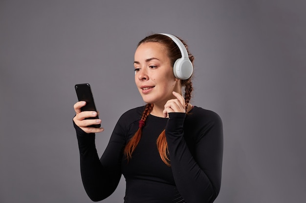 close up portrait of caucasian female podcast or music listening on grey background. listening music in headphones