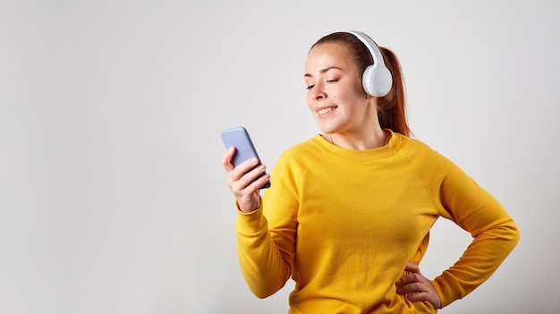 Close up portrait of caucasian female podcast or music listening on grey background. listening music in headphones