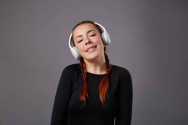 Close up portrait of caucasian female podcast or music listening on grey background. listening music in headphones