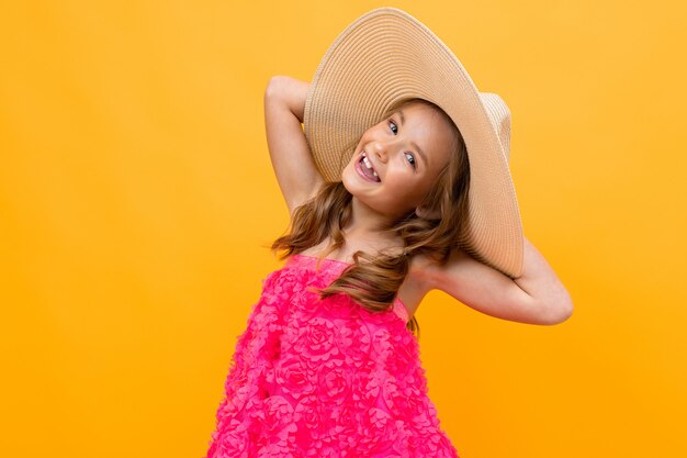 Close-up portrait of a charming cute young child with a straw hat on a yellow background