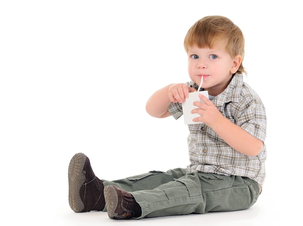 Close-up portrait of a charming little boy drinking fruit juice from a straw on a white background