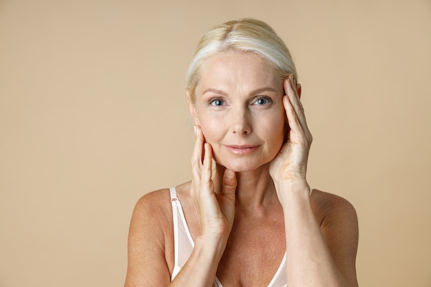 Close up portrait of charming mature woman with blonde hair in white underwear looking at camera