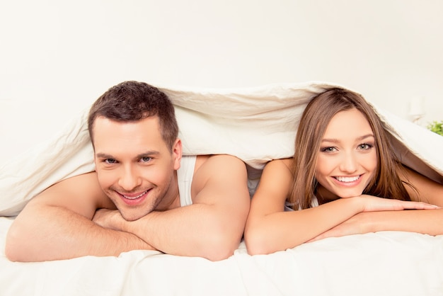 Close up portrait of cheerful couple lying under blanket