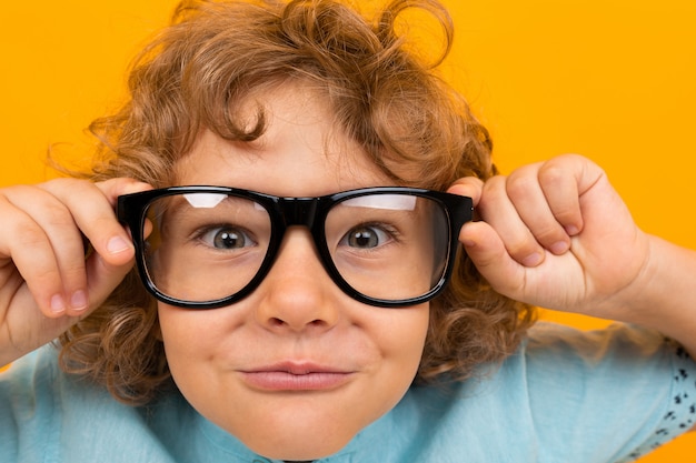 Close-up portrait of a child in glasses for vision on an orange 