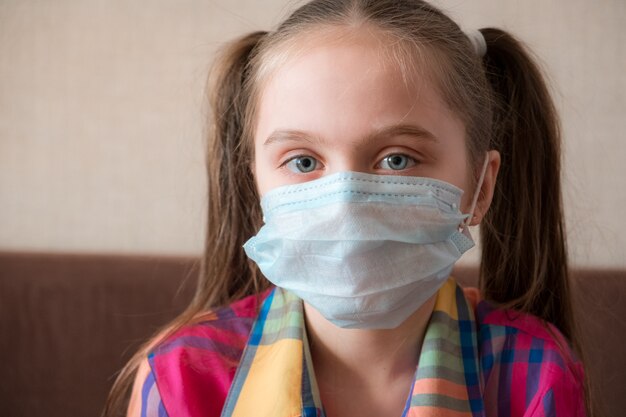 Close-up portrait. Concept of coronavirus quarantine. Child wearing medical protective face mask during flu virus, making stop gesture. COVID-19 - home self isolation.