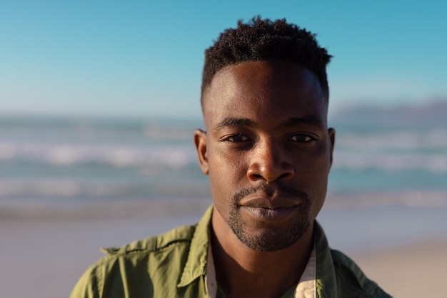 Close-up portrait of confident handsome african american young man against sea and sky at sunset