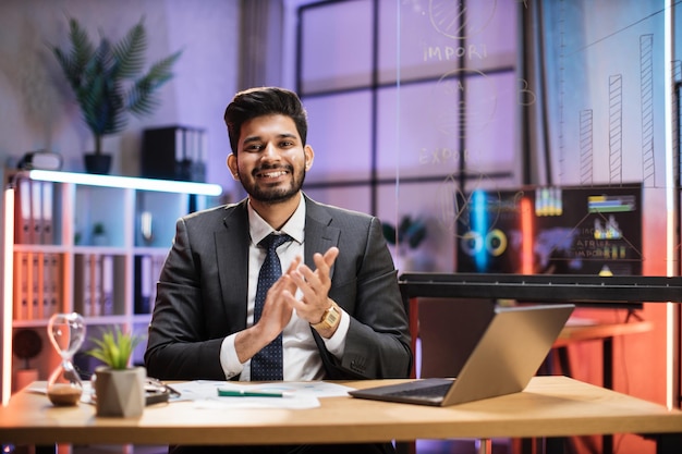 Close up portrait of confident indian financial expert office worker sitting at table in formal suit