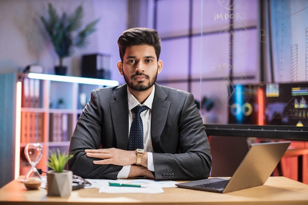 Close up portrait of confident indian financial expert office worker sitting at table in formal suit