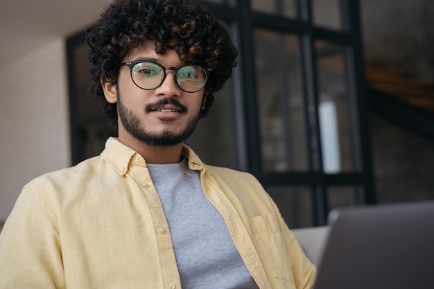 Close up portrait of confident Indian IT specialist using laptop computer working from home