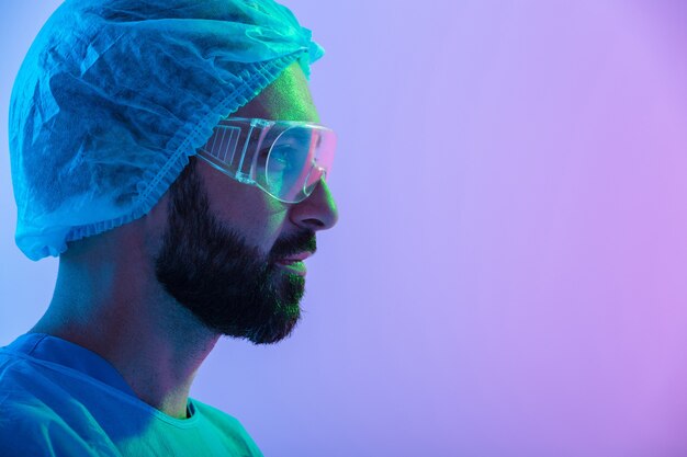 close up portrait of a confident man scientist wearing unifrom and glasses standing isolated over blue-pink haze , looking away