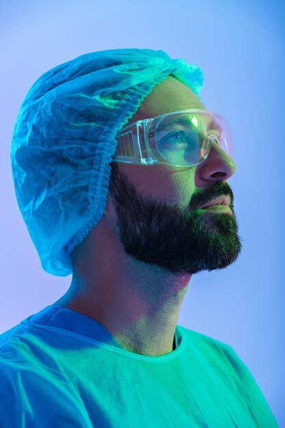 close up portrait of a confident man scientist wearing unifrom and glasses standing isolated over blue-pink haze , looking up
