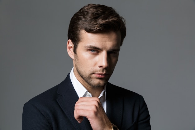 Close up portrait of a confident young businessman dressed in suit isolated over gray wall