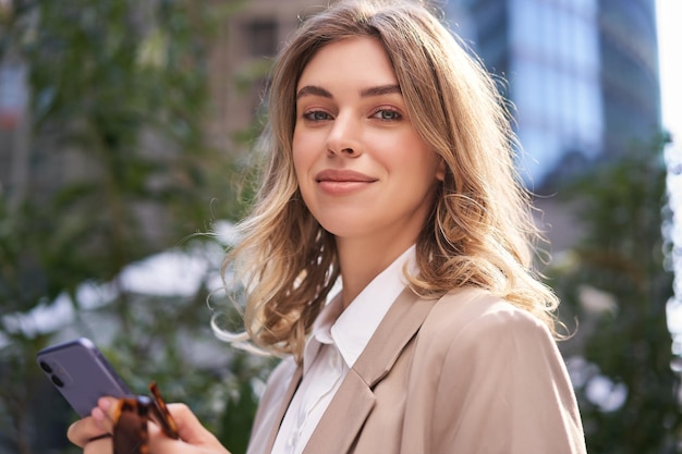 Close up portrait of corporate woman young intern walks on street to office holds mobile phone texts