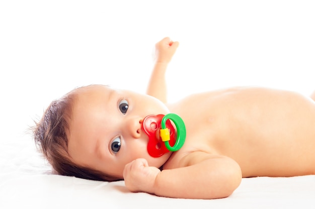 Close-up portrait of a curious little pretty girl lying on a divan and playing with a rattle on a white background. The concept of development of babies and care. Copyspace