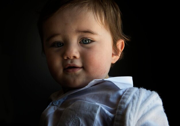 Foto ritratto da vicino di un bambino carino con gli occhi grigi su uno sfondo nero