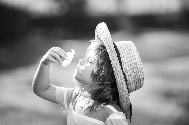 プルメリアの花の子供時代と親の匂いをかぐ麦わら帽子のかわいい小さな子供の肖像画をクローズアップ