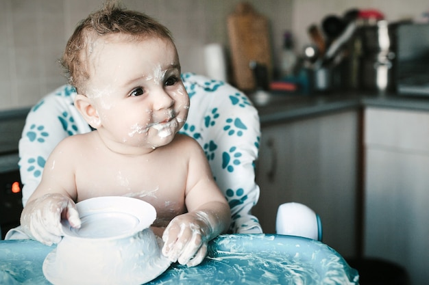 Close up portrait of cute messy baby who eats sweet dessert for the first time.