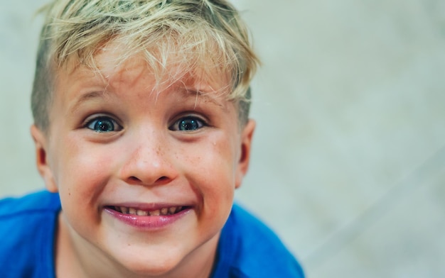 Close up portrait cute smiling blue eyed freckled blond boy artistic facial expressions gestures funny mischievous in happy mood Childhood children education psychology behaviour problems concept