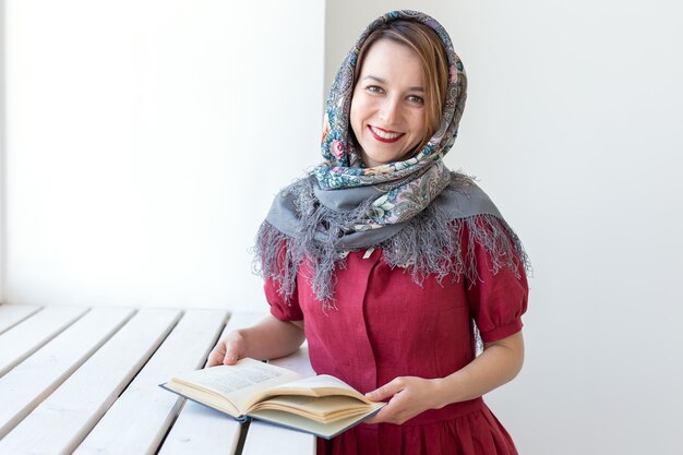 Close-up portrait of a cute young dreamy woman with a book in her hand looking out of the window