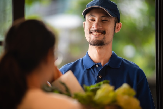 配達員の肖像画、青いTシャツの制服を着た笑顔の男、オンラインショッピングの食料品、新しい通常のライフスタイルコンセプト、小売店のeコマース、都市生活、配達輸送をクローズアップします。