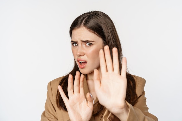 Close up portrait of disgusted, shocked woman cringe, turn away and blocking from something disgusting, standing against white background