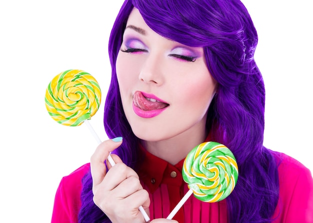 Крупный план портрета мечтающей женщины с фиолетовыми волосами, держащей разноцветные леденцы на палочке и облизывающей губы
