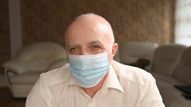 Крупным планом портрет пожилого седого человека в медицинской маске на лице, чтобы защитить себя. Коронавирус пандемия.
