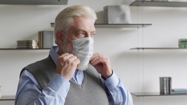 Close up portrait elderly man puts a medical mask on his face to protecting yourself from coronavirus pandemic