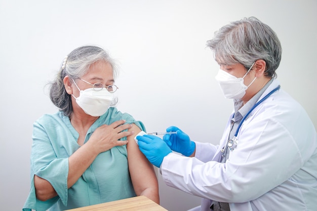 Close-up portrait of an elderly woman receiving coronavirus vaccination from a male doctor wearing blue gloves To strengthen the immune system to prevent infection. Elderly Vaccination