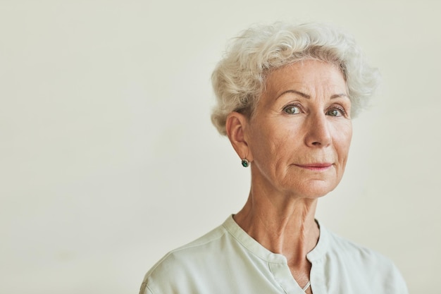 Close up portrait of elegant senior woman looking at camera while standing against neutral backgroun...