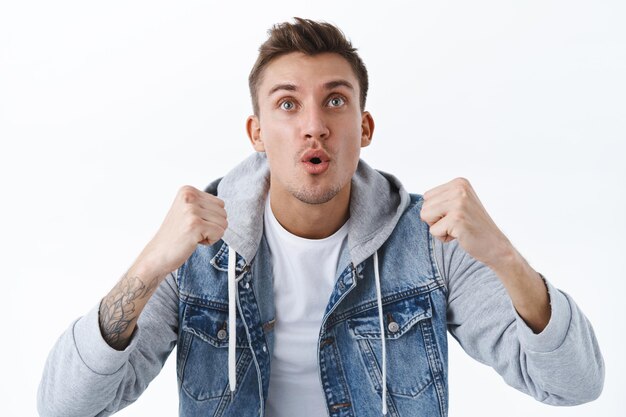 Close-up portrait of excited and amused blond young man watching sport game on tv screen