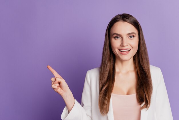 Close up portrait of excited promoter lady direct finger empty space wear formal suit posing on purple wall