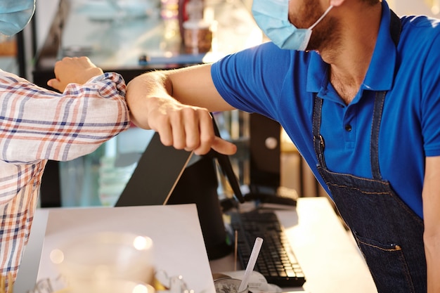 Close-up portrait of female customer giving elbow bump to coffeeshop barista