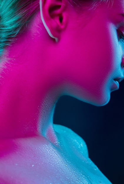 Close up portrait of female fashion model in neon light on dark studio background.