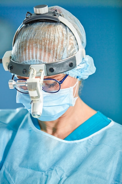 Close up portrait of female surgeon doctor wearing protective mask and hat during the operation. Healthcare, medical education, surgery concept.