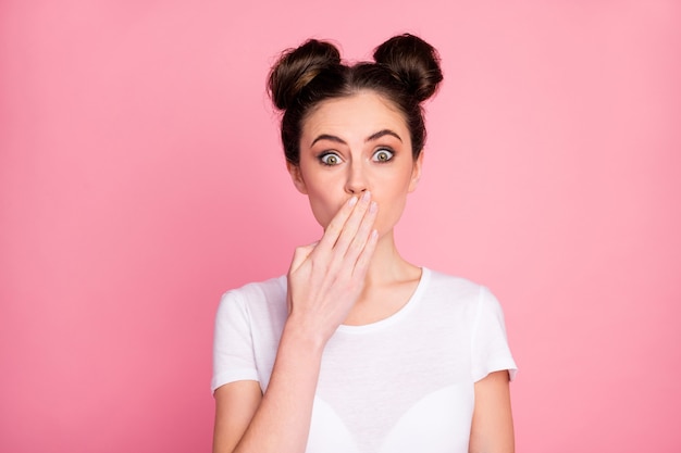 Close-up portrait of funny girl closing mouth with palm isolated over pink background