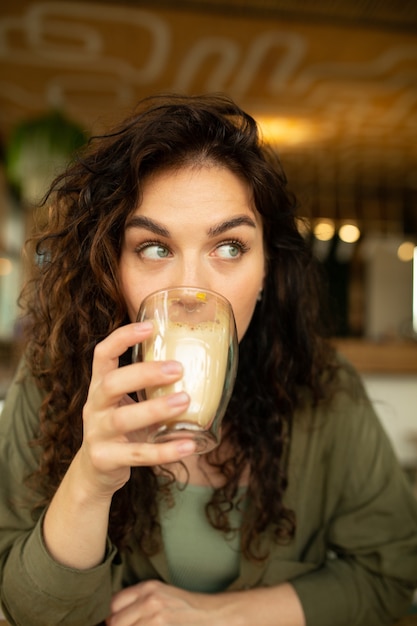 巻き毛の若いきれいな女性の肖像画面白い幸せそうな顔をクローズアップコーヒーショップで飲んでコーヒーを楽しんでいます