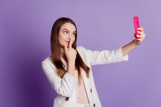 Close up portrait of funny lady hold cellphone make selfie wear formal suit posing on violet wall