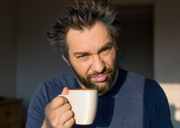 Close up portrait of a funny man after awakening with a big cup. Close up portrait.